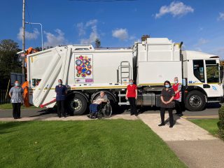 Staff and a resident from Fairways Care Home stand in front of the bin lorry with their artwork on.