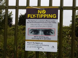 A 'no fly-tipping' warning sign attached to a metal fence.