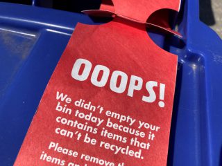 A contamination tag attached to the handle of a blue recycling bin.