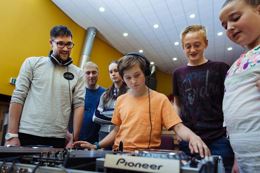Young child at a mixing desk, surrounded by others