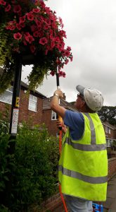 A volunteer from Old Clee in Bloom watering flowers in a basket.