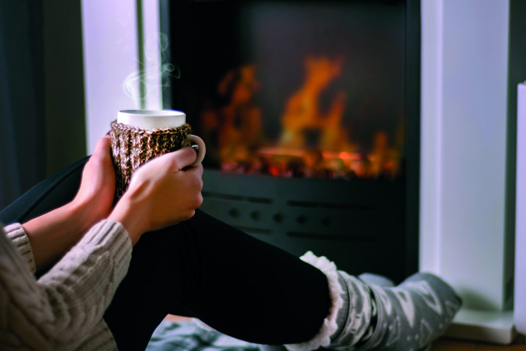 Woman sitting in front of the fireplace and holding cup of tea in hand on legs