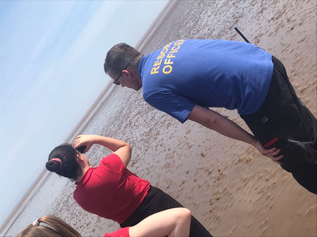 School girl uses binoculars to look out to sea with resort safety officer