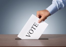 Image of a hand holding a card with writing on it "VOTE"