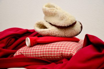 A pile of slippers, blanket, hot water bottle and cushion.