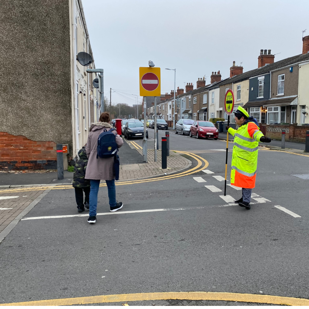 Lollipop lady Josie Hides helps a parent and child cross the road.