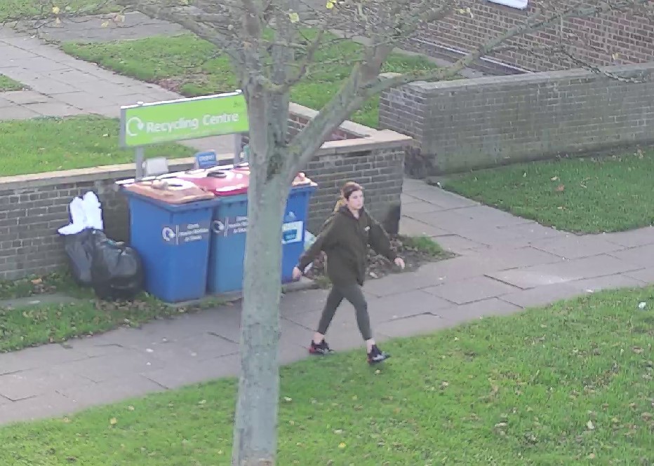 A person walking near some bins