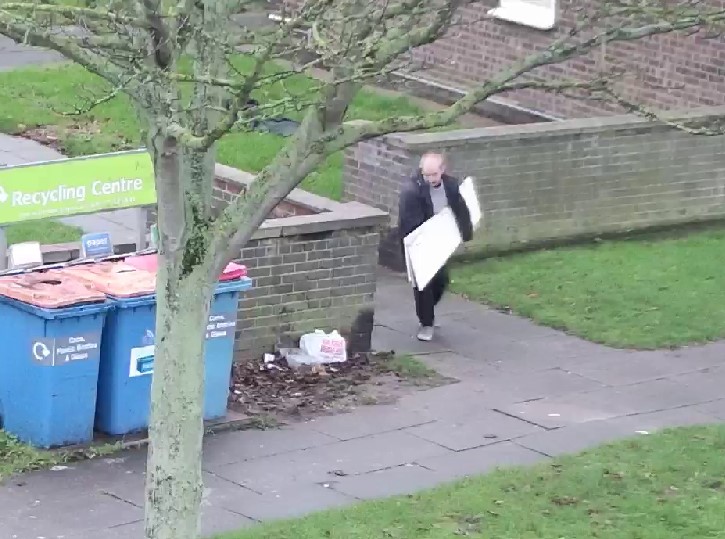 A person carrying a bulky item near some bins