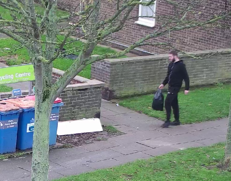 A man carrying a black bag towards a bin.