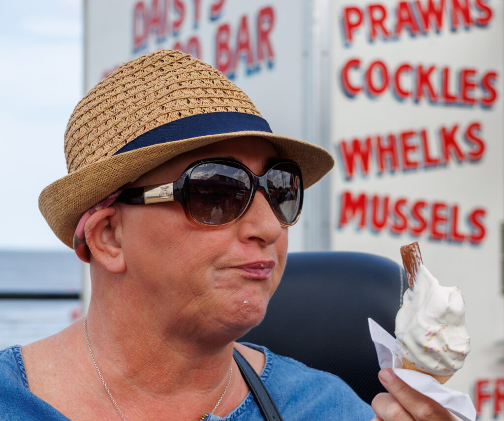 A lady in hat and sunglasses eats an ice cream