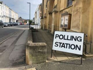 A polling station sign outside a building next to a junction