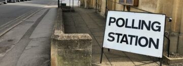 A polling station sign outside a building next to a junction