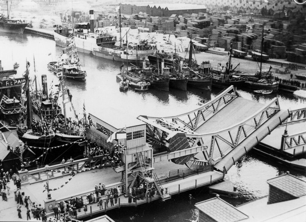 Corporation Bridge, decorated with banners and bunting, opens as crowds try to catch a glimpse of the Prince. A banner hanging from the Control Room reads: Greetings to our Empire's Ambassador