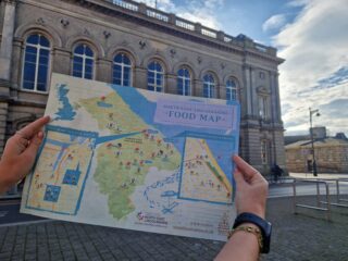 A person holding the North East Lincolnshire Food Map with Grimsby Town Hall in the background
