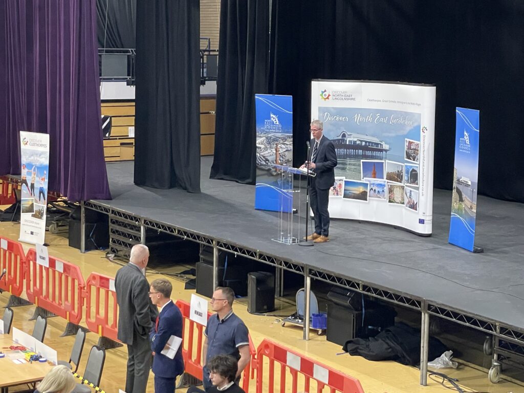 A photo of Returning Officer, Rob Walsh, announcing that four wards had completed verification.