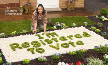 Woman in a garden in front of flower bed that spells out "I'm registered to vote"