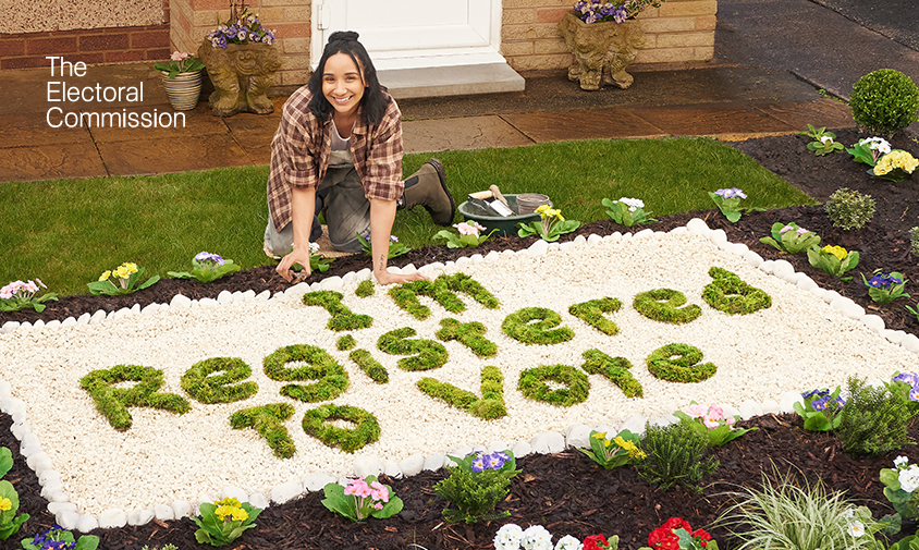 Woman in a garden in front of flower bed that spells out "I'm registered to vote"