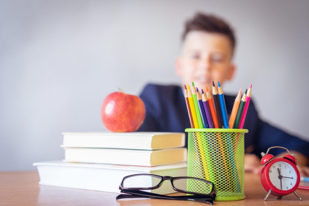Boy sat at a desk behind books, pencils and an apple