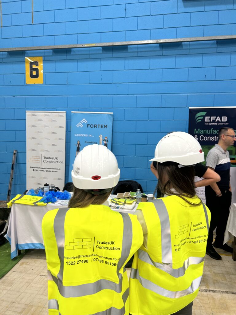 Young adults wearing a hard hat and yellow hi vis jacket at a careers event for construction