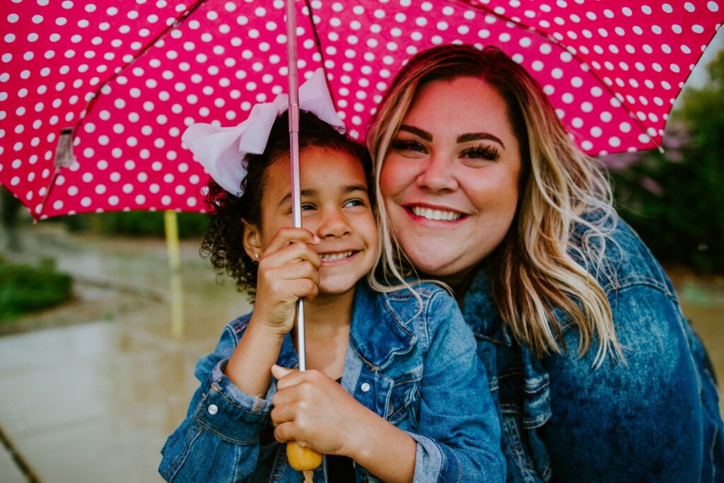 Woman and young girl smiling underneath an umbrella