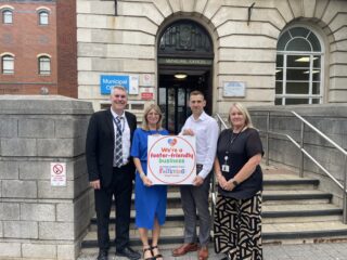 A photo of NELC and Navigo representatives with a foster-friendly business sign.