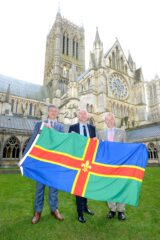 A photo of the leaders of the three Lincolnshire local authorities standing outside the cathedral with a Lincolnshire flag