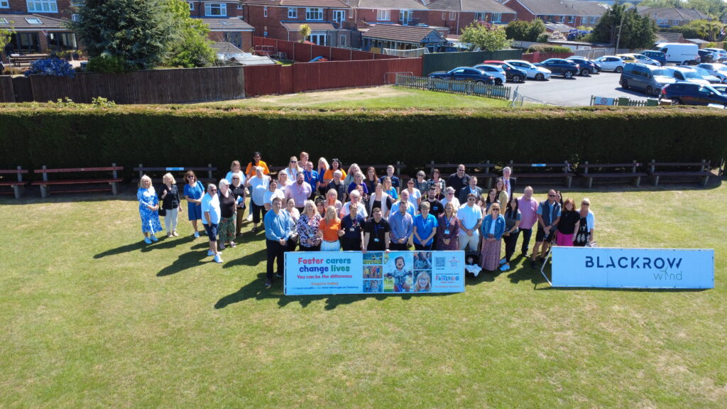 A group photo taken from a drone with around 40 people stood around a Fostering NELC banner