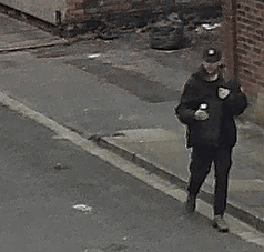 A man wearing a black puffer coat and black cap walking down Harold Street in Grimsby whilst holding a tin can