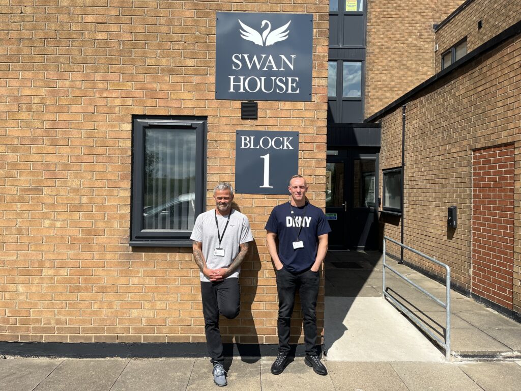 Two men stood in front of a building underneath a sign that says Swan House Block 1