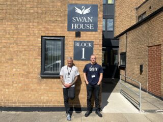Two men stood in front of a building underneath a sign that says Swan House Block 1