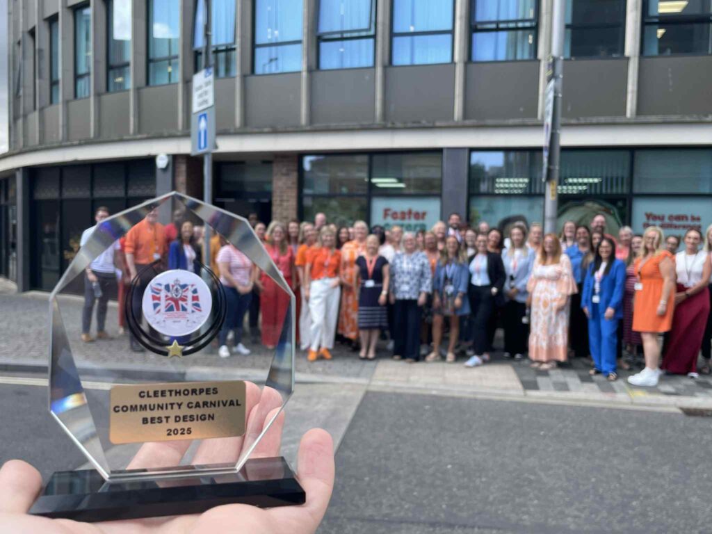 A photo of a glass trophy held up in the foreground, with people gathered behind it.