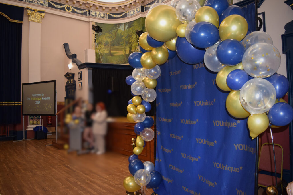 A blue and gold balloon arch with a photo backdrop in the town hall Grimsby