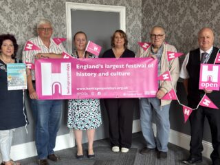 A photo of six people holding a banner and some bunting.