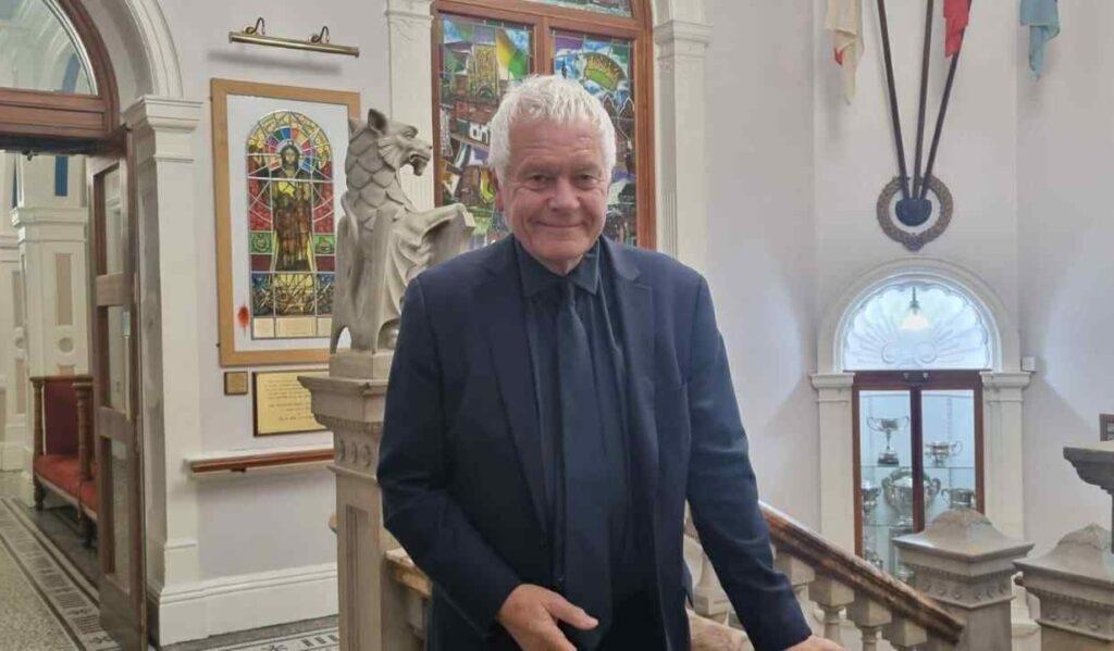 A photo of a man leaning on a stair banister, smiling.