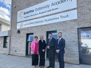 Representatives from Scartho Gateway Academy and North East Lincolnshire Council stand outside the new school building under a sign