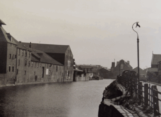 A black and white photo of some buildings along a river bank.