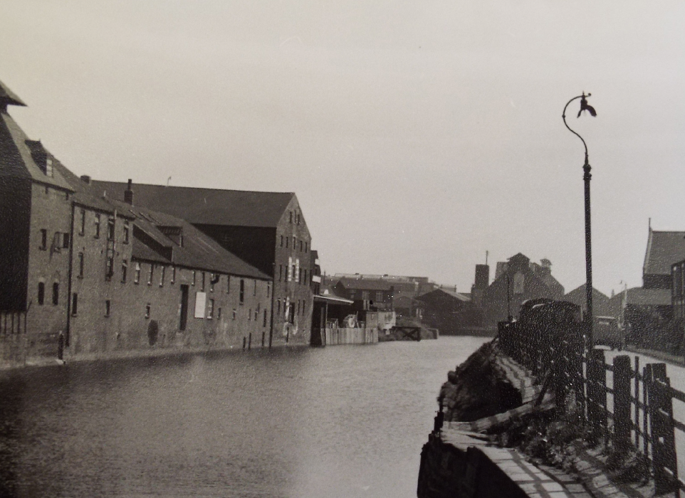 A black and white photo of some buildings along a river bank.