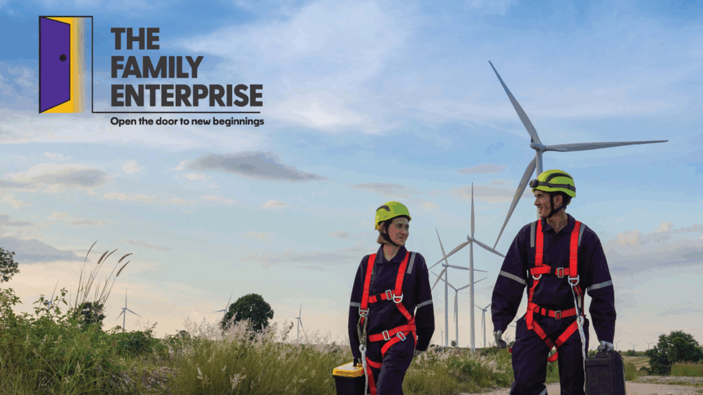 Two people walking next to a wind turbine