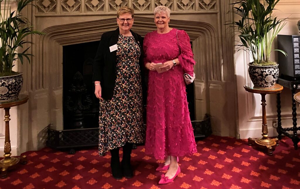 A photo of two people standing in a large room in front of a fire place