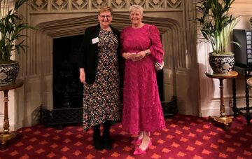 A photo of two people standing in a large room in front of a fire place