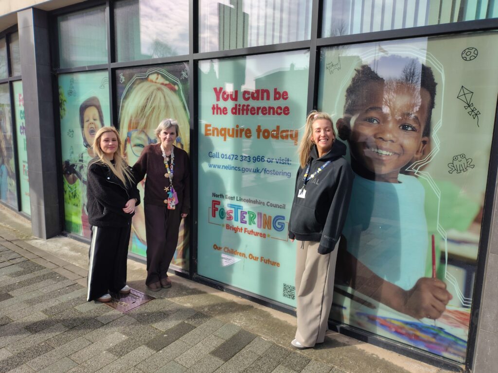 A photo of three women in front of a fostering advert