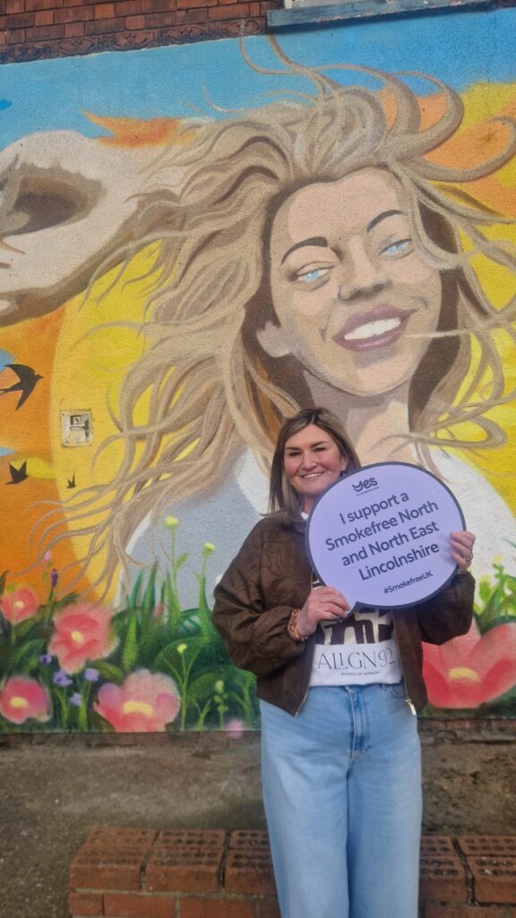 Wendy Robinson in front of the stop smoking mural with a smokefree sign.