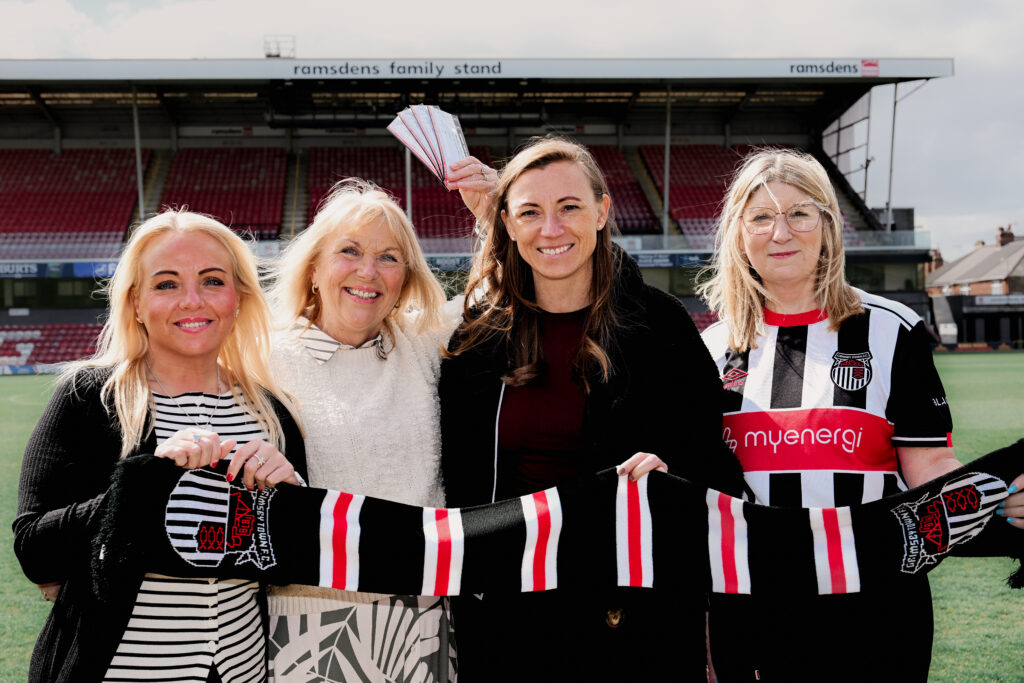 Foster Carers Kerry and Deb, CEO of GTFC Polly Bancroft and Director of Children's Services Ann-Marie Matson pose with a GTFC scarf at Blundell Park