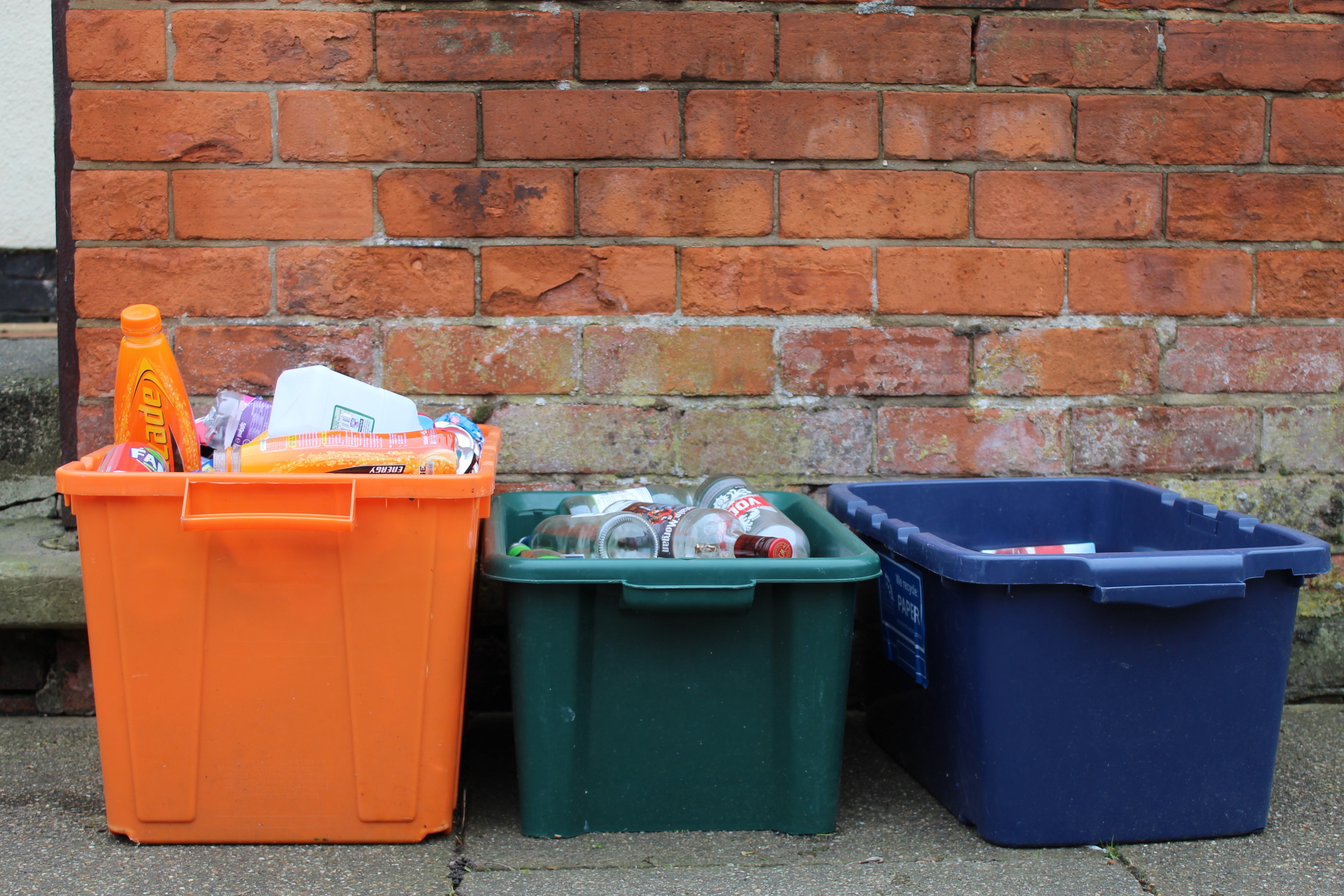 Three recycling boxes in front of a brick wall.